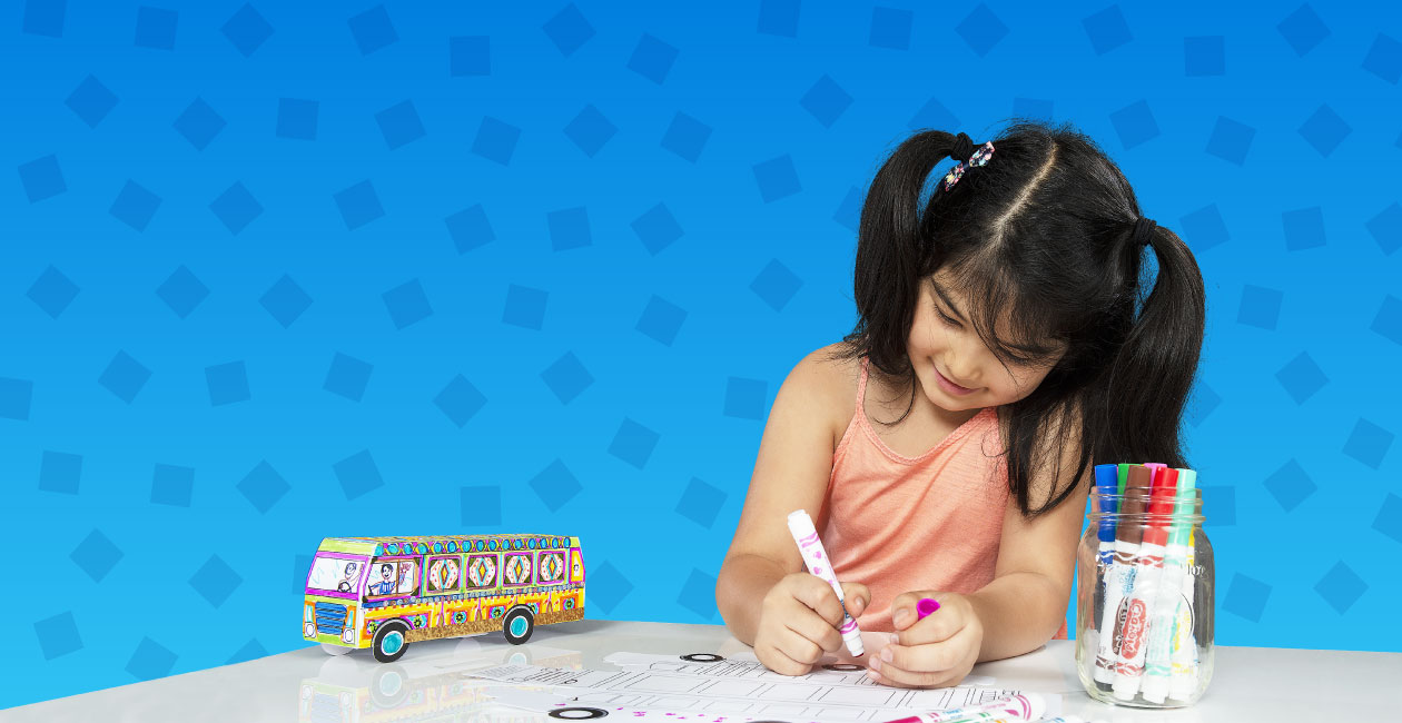 Girl coloring a Crayola Imagine Arts Academy bus take home while a completed version is next to her on the table. Image is on